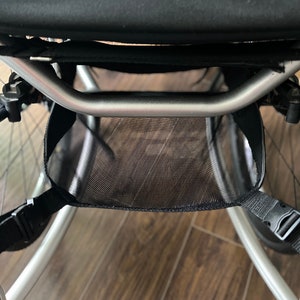 Puede incluir: Un cochecito plateado con una cesta de almacenamiento de malla negra debajo del asiento.