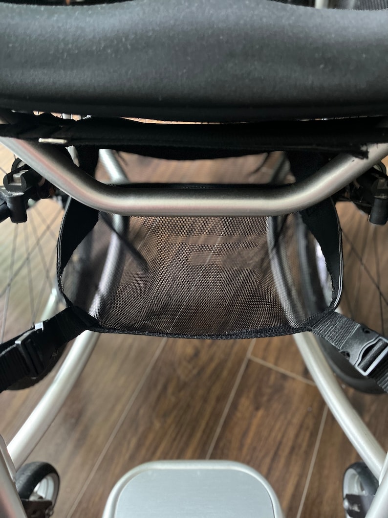 Peut inclure: Une poussette argent&eacute;e avec un panier de rangement en maille noire sous le si&egrave;ge.