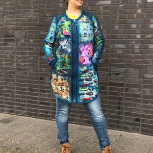 May include: A long blue denim jacket with a colourful print featuring animals, flowers, and cars. The jacket has a zip closure and two pockets.