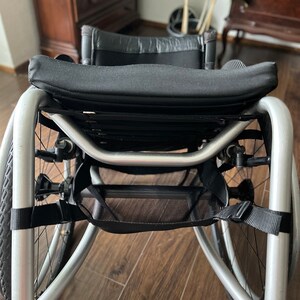 Peut inclure: Un fauteuil roulant argent&eacute; avec un si&egrave;ge et un dossier en tissu noir, un sac de rangement en maille noire et des sangles noires.