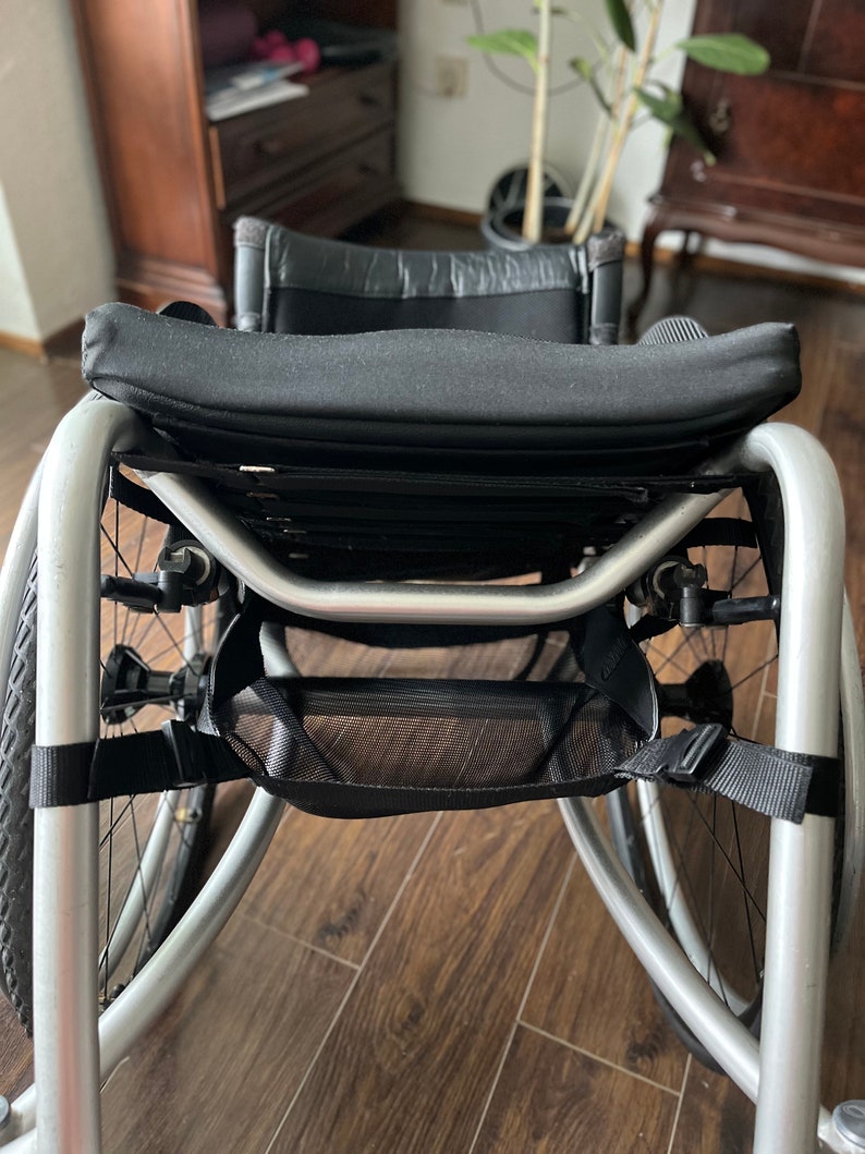 Peut inclure: Un fauteuil roulant argent&eacute; avec un si&egrave;ge et un dossier en tissu noir, un sac de rangement en maille noire et des sangles noires.