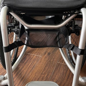 Peut inclure: Un fauteuil roulant argent&eacute; avec un si&egrave;ge et un dossier en tissu noir, un sac de rangement en maille noire et un repose-pieds argent&eacute;.