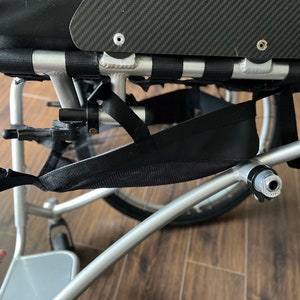 Peut inclure: Un fauteuil roulant argent&eacute; avec un sac de rangement en maille noire fix&eacute; au cadre. Le fauteuil roulant a un si&egrave;ge noir et un dossier en fibre de carbone.