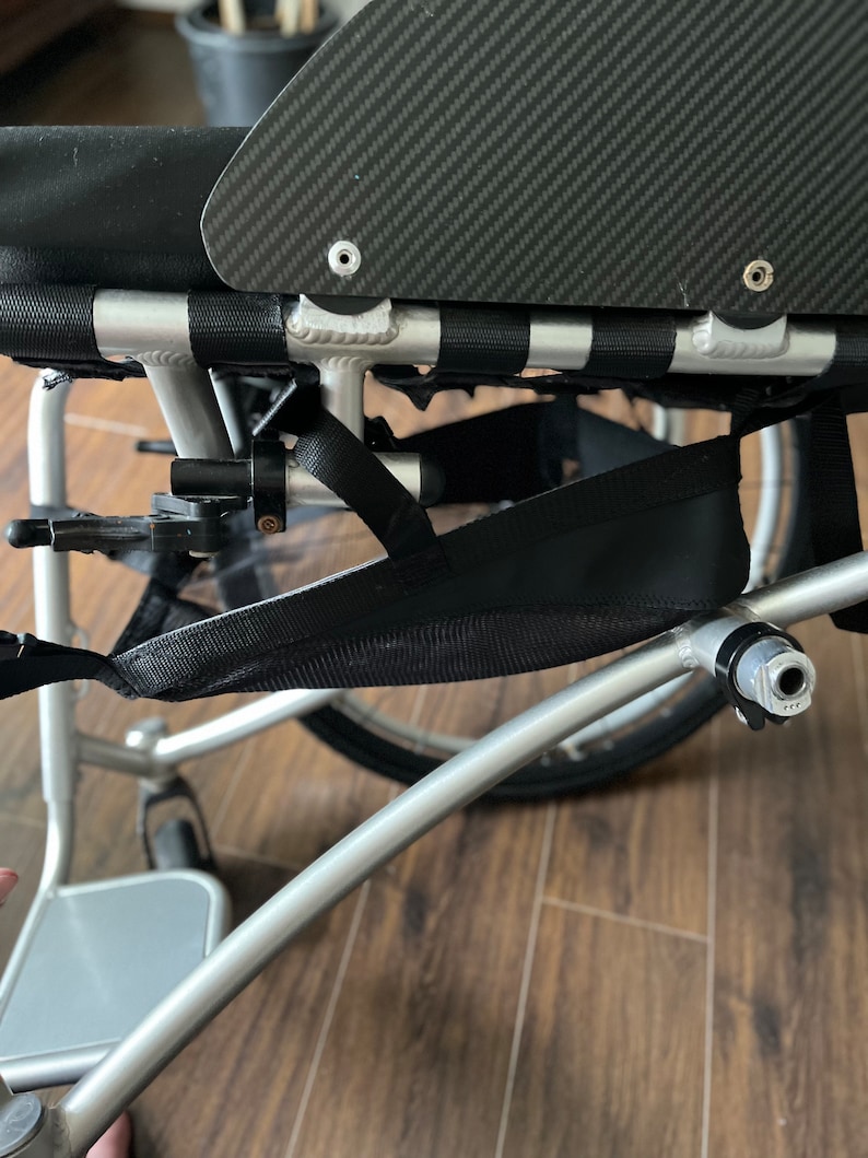 Peut inclure: Un fauteuil roulant argent&eacute; avec un sac de rangement en maille noire fix&eacute; au cadre. Le fauteuil roulant a un si&egrave;ge noir et un dossier en fibre de carbone.