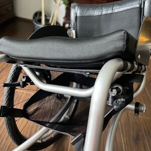 Peut inclure: Un fauteuil roulant argent&eacute; avec un sac de rangement en maille noire et un si&egrave;ge rembourr&eacute; noir. Le fauteuil roulant a un dossier rembourr&eacute; noir et une poign&eacute;e noire.
