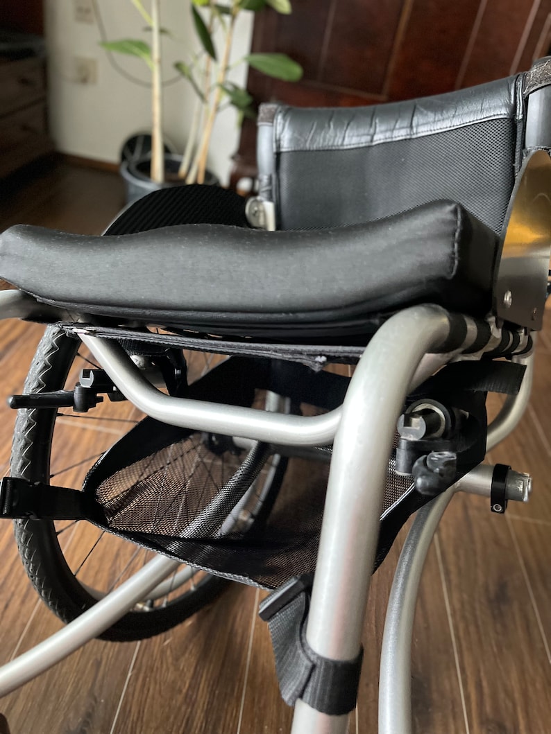 Peut inclure: Un fauteuil roulant argent&eacute; avec un sac de rangement en maille noire et un si&egrave;ge rembourr&eacute; noir. Le fauteuil roulant a un dossier rembourr&eacute; noir et une poign&eacute;e noire.