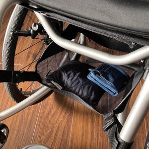Peut inclure: Un fauteuil roulant argent&eacute; avec un sac de rangement en maille noire sous le si&egrave;ge. Le sac contient une pochette matelass&eacute;e noire et un portefeuille bleu. Le fauteuil roulant a un repose-pieds argent&eacute;.