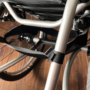 Peut inclure: Un fauteuil roulant argent&eacute; avec un sac de rangement en maille noire fix&eacute; au cadre. Le fauteuil roulant a un si&egrave;ge rembourr&eacute; noir et un repose-pieds.