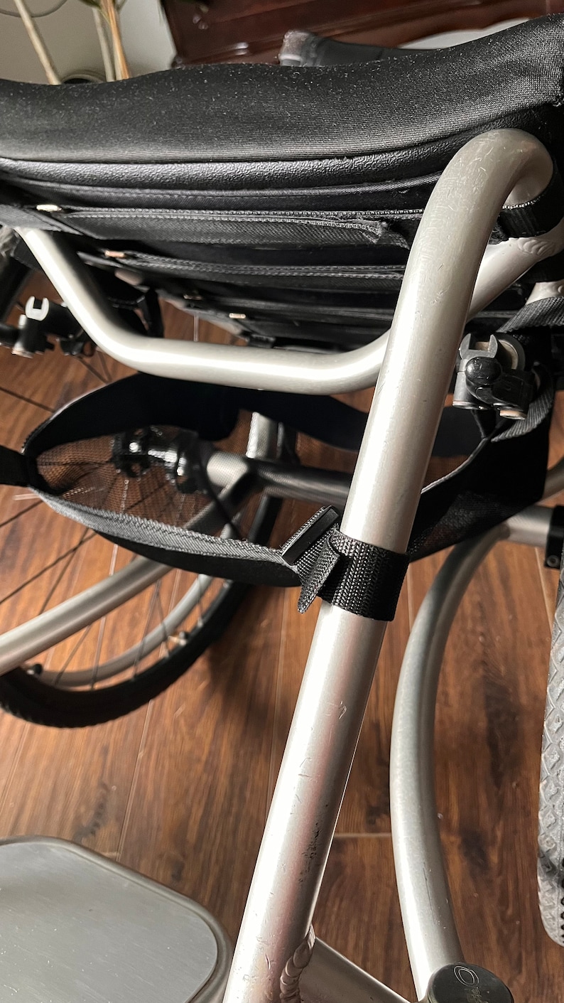 Peut inclure: Un fauteuil roulant argent&eacute; avec un sac de rangement en maille noire fix&eacute; au cadre. Le fauteuil roulant a un si&egrave;ge rembourr&eacute; noir et un repose-pieds.