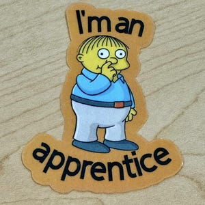 May include: A sticker featuring a cartoon character with yellow skin, blue shirt, and white pants. The text "I'm an apprentice" is written on the sticker.