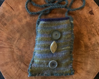 May include: A small, hand-knitted pouch in shades of green, blue, and gray, with a dark blue strap. The pouch is adorned with three decorative buttons: two round and one leaf-shaped.