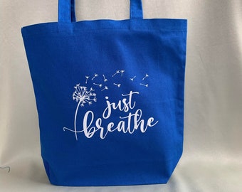 May include: A blue canvas tote bag with white text that reads "just breathe" and a white dandelion graphic.