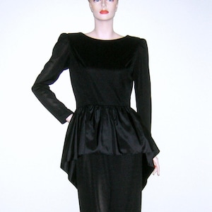 May include: A black dress with a fitted bodice and a high, round neckline. The dress has a peplum waist and a skirt that falls to the knees. The dress is made of a smooth, silky fabric.