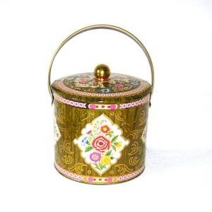 May include: A decorative, vintage tin container with a lid and handle. The olive green tin features floral designs and a gold handle. The lid and sides are adorned with colorful flowers and ornate patterns, adding a touch of elegance.