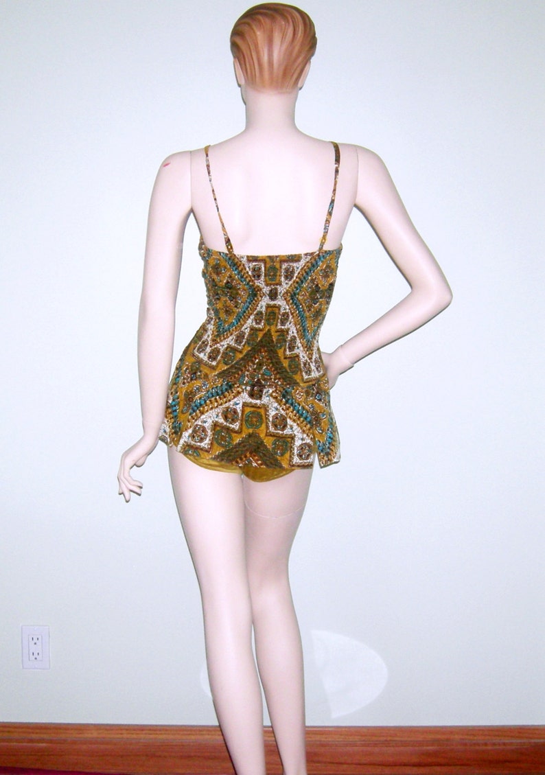 May include: A brown and green patterned swimsuit with a geometric design. The swimsuit has thin straps and a fitted bodice.
