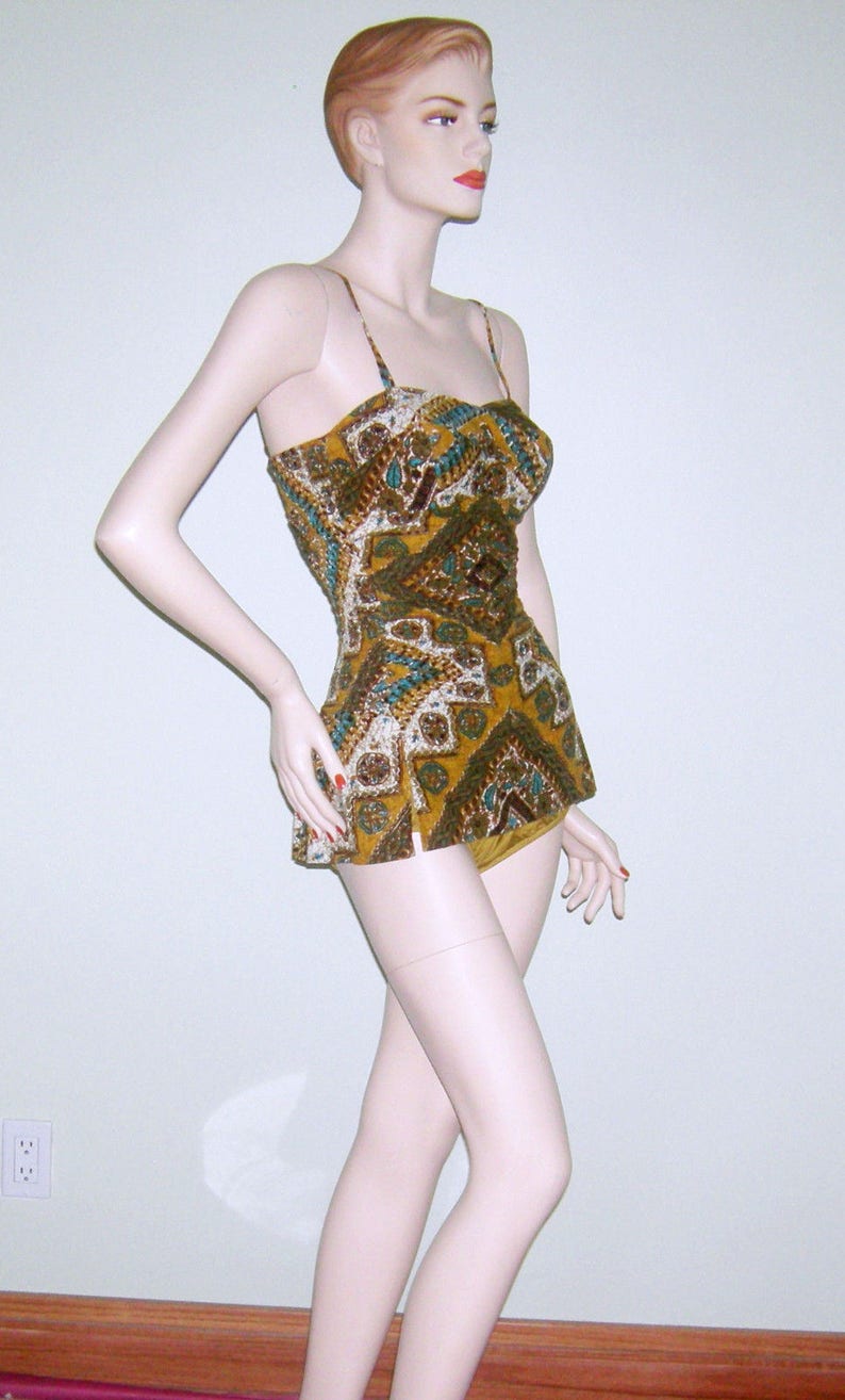 May include: A vintage swimsuit with a geometric pattern in shades of brown, gold, and teal. The swimsuit has a fitted bodice and a full skirt.