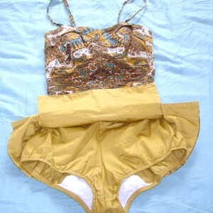 May include: A vintage swimsuit with a brown and blue paisley print top and a solid mustard yellow bottom. The swimsuit has a gathered skirt and a white lining.