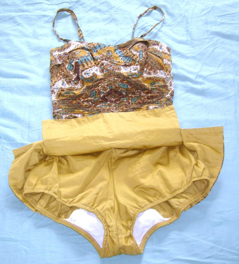 May include: A vintage swimsuit with a brown and blue paisley print top and a solid mustard yellow bottom. The swimsuit has a gathered skirt and a white lining.