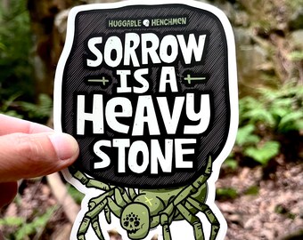 May include: A black and white sticker with a spider carrying a heavy stone. The stone has the text "SORROW IS A HEAVY STONE" on it. The sticker is from the company "Huggable Henchmen".