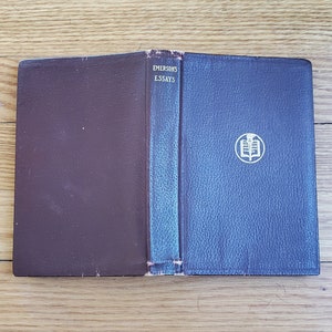 May include: A closed book with a brown leather cover and a blue leather spine. The spine has the title "EMERSON'S ESSAYS" printed in gold lettering. The book has a gold embossed design on the front cover.