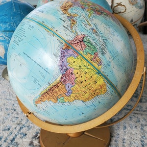 May include: A blue globe with a gold stand, showing the continents of North and South America. The globe has a detailed map with country borders and names. The globe is on a white rug.