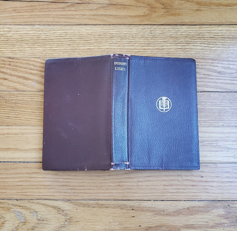 May include: A closed book with a brown leather cover and a blue leather spine. The spine has the title "EMERSON'S ESSAYS" printed in gold lettering. The book has a gold embossed design on the front cover.