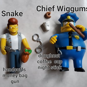 May include: Two action figures of characters from The Simpsons. One figure is Snake, holding a gun and a money bag. The other is Chief Wiggums, holding a night stick. Accessories include handcuffs, a coffee cup, and a donut.