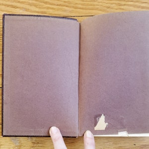 May include: A brown leather-bound book with a blank page open. The book is lying flat on a wooden surface.