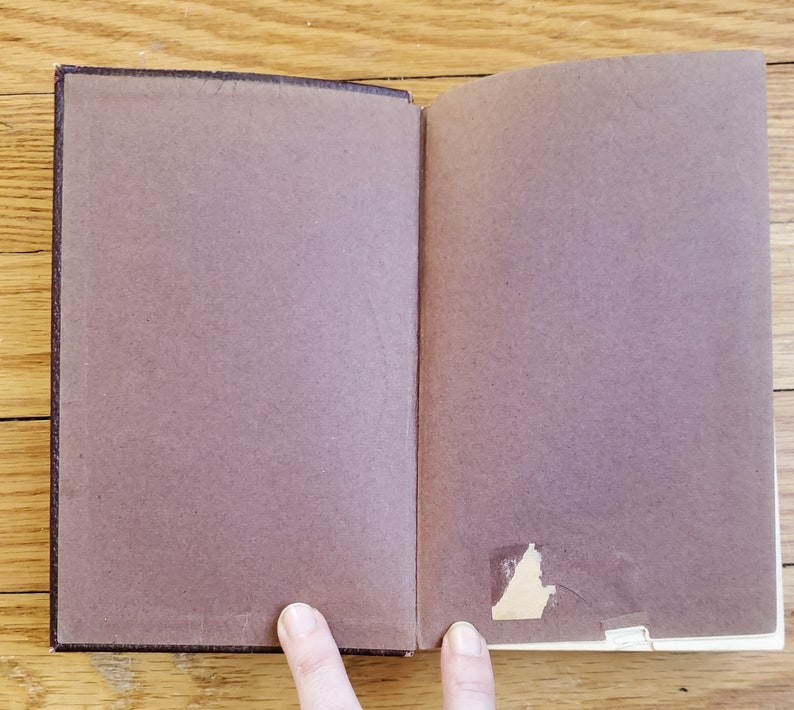 May include: A brown leather-bound book with a blank page open. The book is lying flat on a wooden surface.