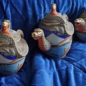 May include: Three decorative ceramic jars with lids, featuring dragon motifs. The jars have a blue, white, and red color scheme with intricate silver-colored metal accents. The dragon heads are prominent on the lids and sides, adding a unique touch to the design.