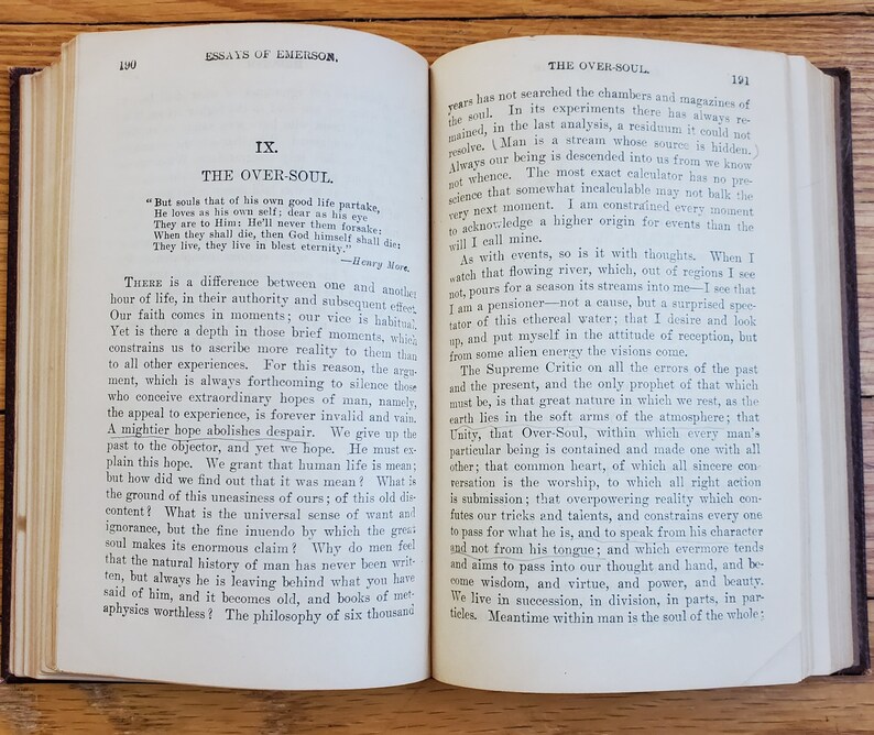 May include: An open book with yellowed pages, showing an excerpt from the essay "The Over-Soul" by Ralph Waldo Emerson. The text discusses the concept of a higher power and the interconnectedness of all things.