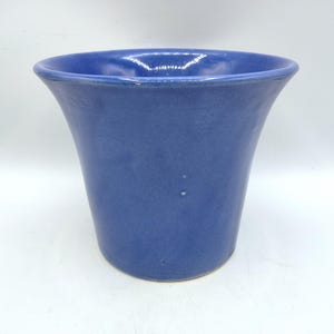 May include: A light blue ceramic planter with a flared rim. The planter is smooth and has a glossy finish.