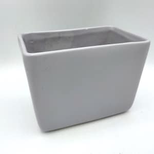May include: A square, light gray ceramic planter with a slightly tapered design. The planter has a smooth, matte finish and is suitable for indoor or outdoor use. The interior is a darker gray.