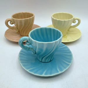 May include: Three ceramic teacups and saucers in pastel colors: peach, yellow, and light blue. Each cup has a spiral design and a curved handle. The saucers have a matching fluted pattern.