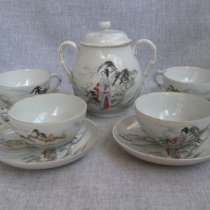 May include: A white porcelain tea set featuring a sugar bowl and four teacups with saucers. Each piece is decorated with a hand-painted landscape scene with figures in red and gold accents. The set has a vintage aesthetic.