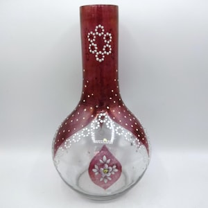May include: A decorative glass vase with a bulbous base and a long neck. The top portion is a deep burgundy color, adorned with white dot and floral patterns. The clear base features a painted floral design.