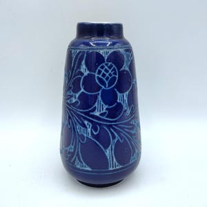 May include: A cobalt blue ceramic vase with a floral design. The vase has a rounded body and a narrow neck. The floral pattern is in a lighter shade of blue, creating a contrast against the darker background. The vase is approximately 8 inches tall.