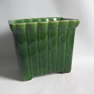 May include: A square, green ceramic planter with a ribbed design. The planter has a glossy finish and a slightly flared top edge. It is a decorative item for indoor or outdoor use.