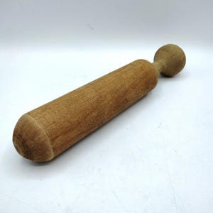 May include: A wooden rolling pin with a cylindrical body and a rounded handle. The rolling pin is made of light brown wood and is designed for rolling out dough. The handle is a small, rounded knob.