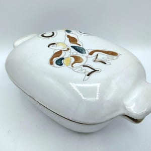 May include: White ceramic serving dish with a lid. The lid is decorated with a butterfly design in brown, yellow, and blue. The dish has a rounded shape with a handle on each side.