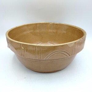 May include: A large, brown ceramic mixing bowl with a decorative rim. The bowl has a smooth, glazed finish and is perfect for mixing ingredients or serving salads.