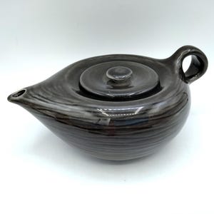 May include: A black ceramic teapot with a lid. The teapot has a unique, wavy design and a spout on the side.