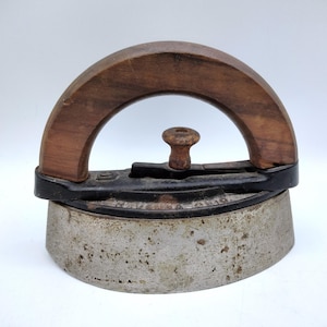May include: Antique flat iron with a wooden handle. The iron has a rounded base and a dark metal frame. The handle is arched and made of polished wood. The iron is a vintage item, likely used for pressing clothes.