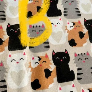 May include: A beige fabric with a repeating pattern of black, white, gray, and brown cats. The cats are all smiling and have different patterns on their fur. The fabric is perfect for crafting projects, such as making pillows, blankets, or tote bags.
