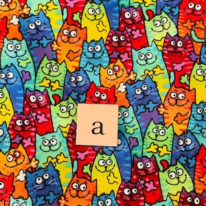 Pode incluir: Um tecido colorido com um padr&atilde;o repetitivo de gatos de desenho animado em v&aacute;rias cores e poses. A letra "a" est&aacute; impressa em um quadrado branco.