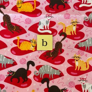 Pode incluir: Tecido rosa com um padr&atilde;o repetido de cora&ccedil;&otilde;es vermelhos e gatos usando &oacute;culos em forma de cora&ccedil;&atilde;o. Os gatos est&atilde;o em v&aacute;rias poses e cores, incluindo laranja, preto, cinza e branco. O tecido tem um fundo rosa com pequenos cora&ccedil;&otilde;es brancos.
