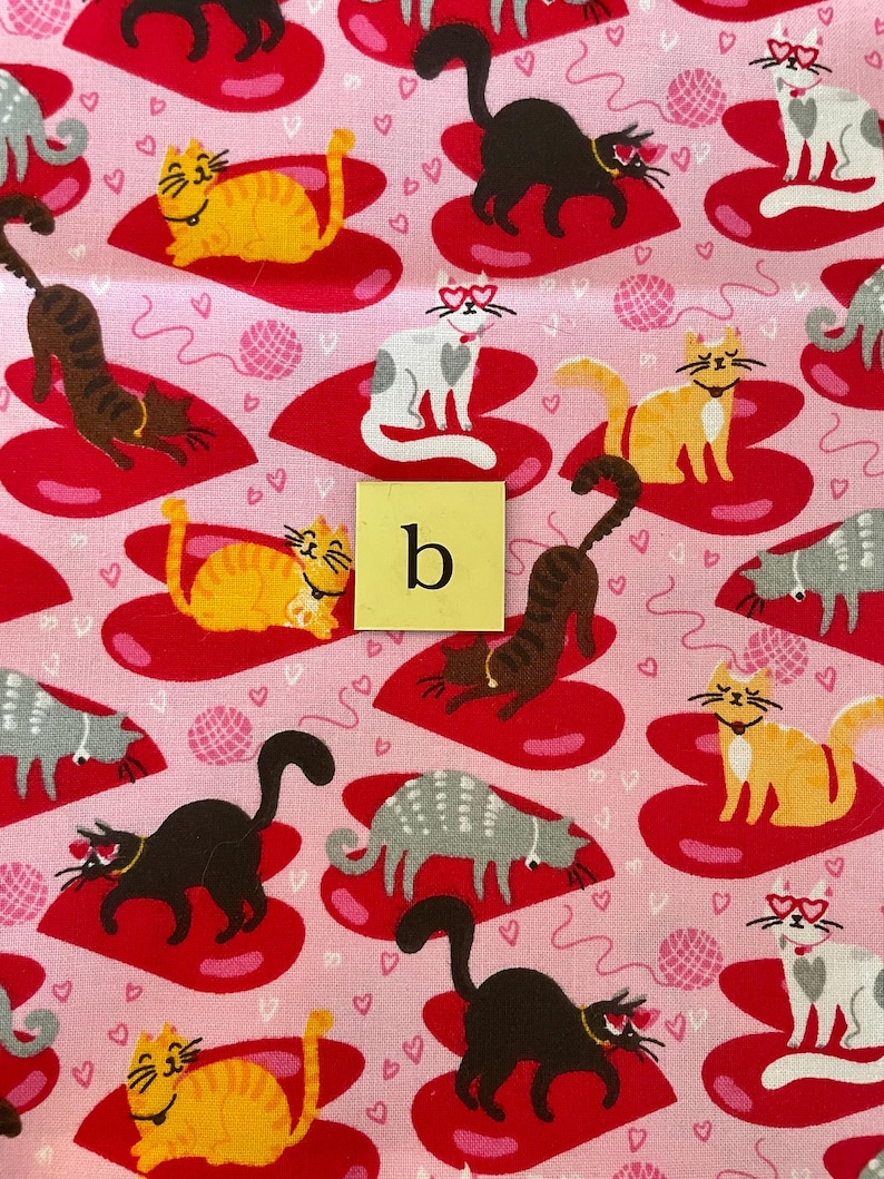 Pode incluir: Tecido rosa com um padr&atilde;o repetido de cora&ccedil;&otilde;es vermelhos e gatos usando &oacute;culos em forma de cora&ccedil;&atilde;o. Os gatos est&atilde;o em v&aacute;rias poses e cores, incluindo laranja, preto, cinza e branco. O tecido tem um fundo rosa com pequenos cora&ccedil;&otilde;es brancos.