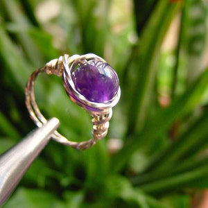 May include: A silver wire wrapped ring with a purple amethyst gemstone.