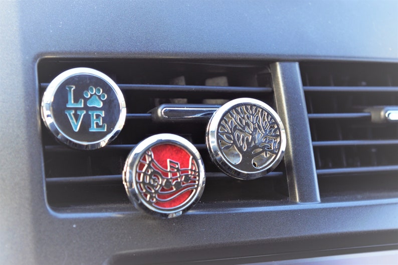 K&ouml;nnte beinhalten: Drei silberne Autolufterfrischer mit verschiedenen Designs. Der erste ist schwarz mit dem Wort "LOVE" und einem Pfotenabdruck. Der zweite ist rot mit einem Musiknoten-Design. Der dritte ist silber mit einem Baumdesign.