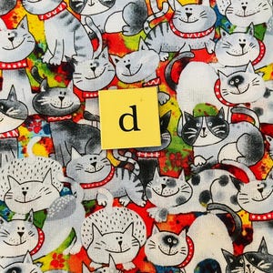 Pode incluir: Um tecido colorido com um padr&atilde;o repetitivo de gatos de desenho animado. Os gatos s&atilde;o desenhados em preto e branco com colares vermelhos e s&atilde;o colocados sobre um fundo de cores brilhantes, incluindo vermelho, amarelo, laranja, verde e azul.